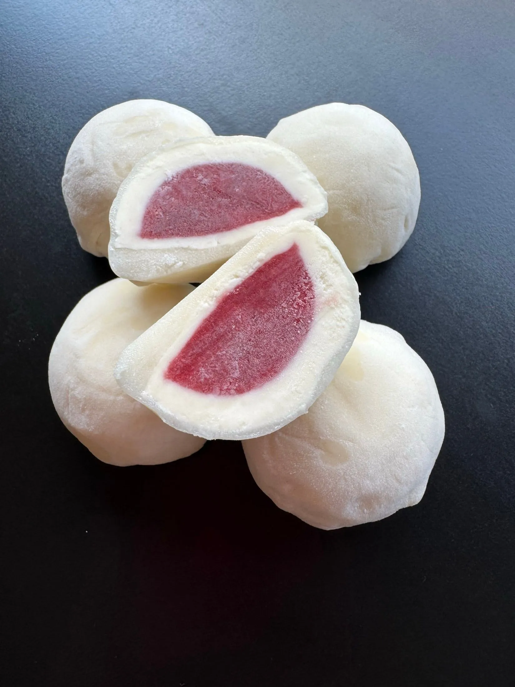 Mochi blancos sobre pizarra negra, dos cortados al medio mostrando el relleno rojo de frutilla